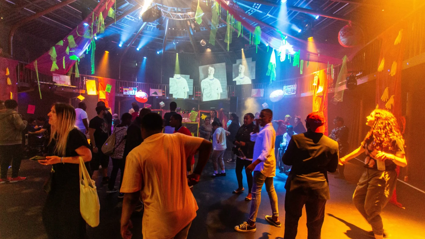 A group of people partying in the Albany theatre, with blue and yellow lighting.