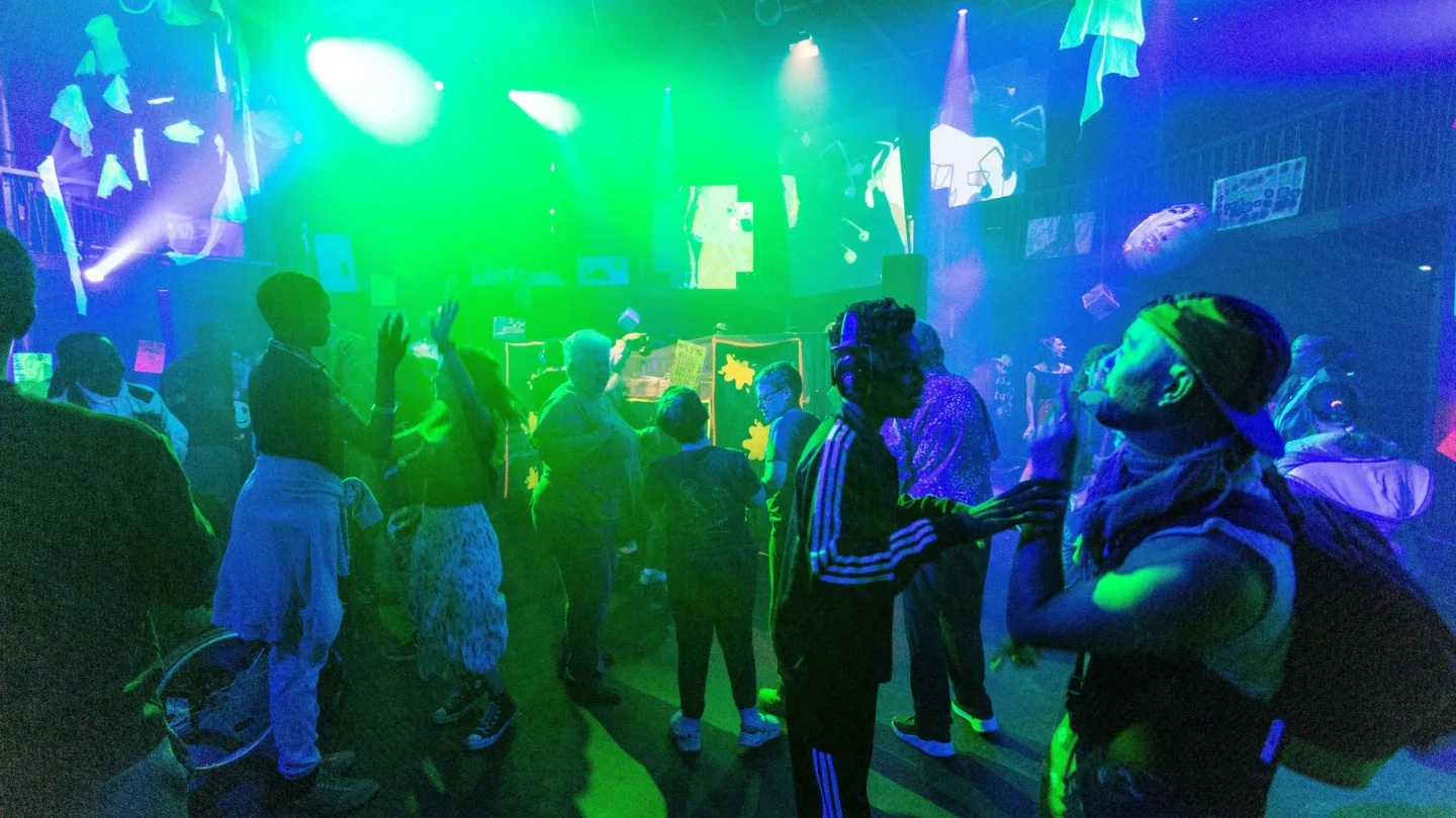 A photo of a group of young people on a dancefloor with blue and green lighting.