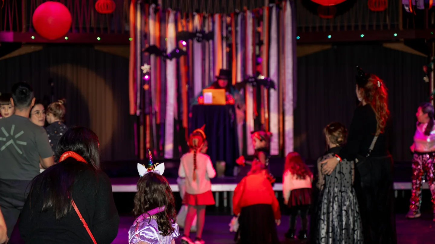 A photo of a dancefloor decorated with streamers and hanging lights, with children and parents dancing in the foreground.