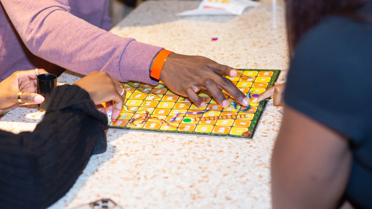 A show of three people's hands playing a game of snakes and ladders.