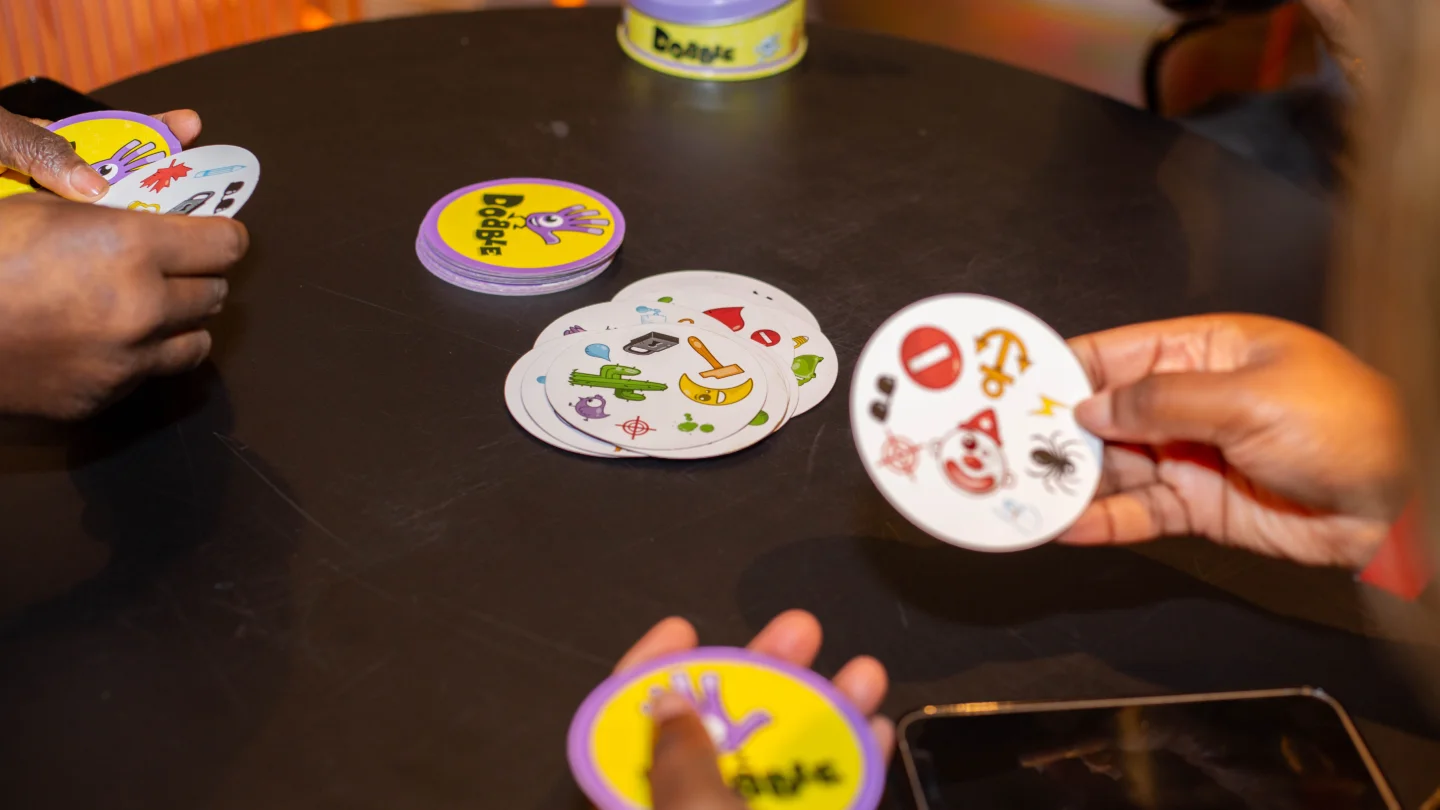 A close up photo of three people's hands playing a game involving circular cards with icons on them.