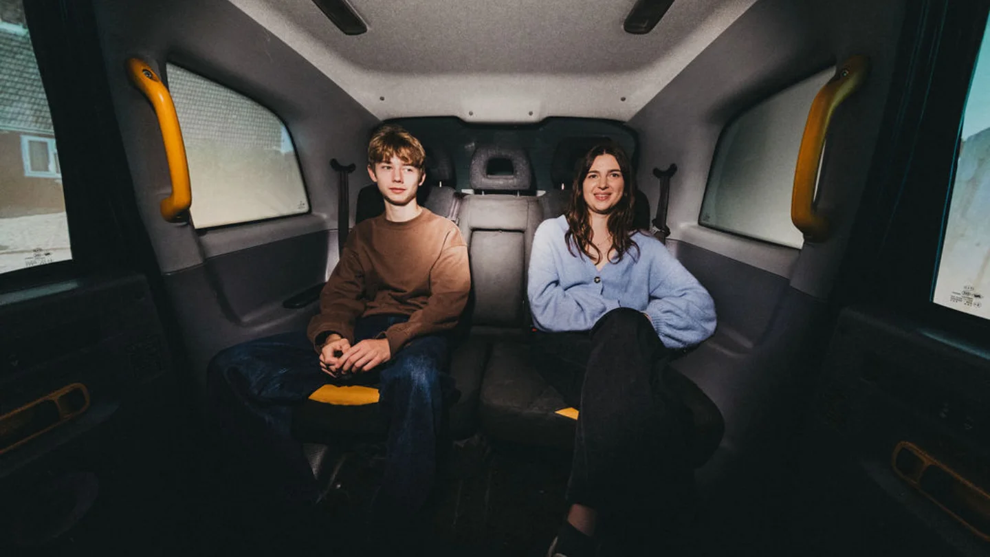A photo of two people, a white man and a white woman, sat in the back of a black cab.