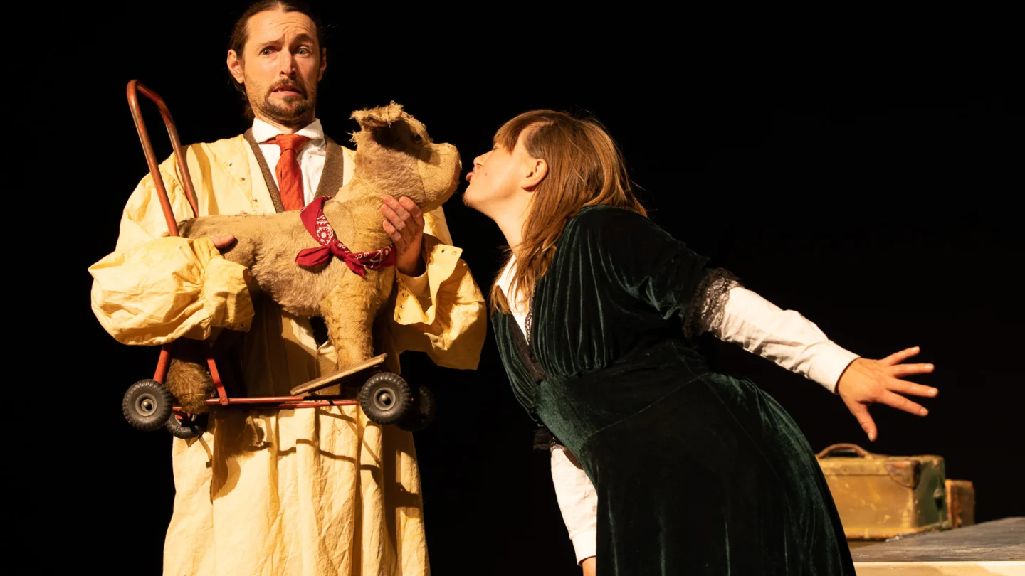 A person holding a toy dog. Another person is kissing the dog