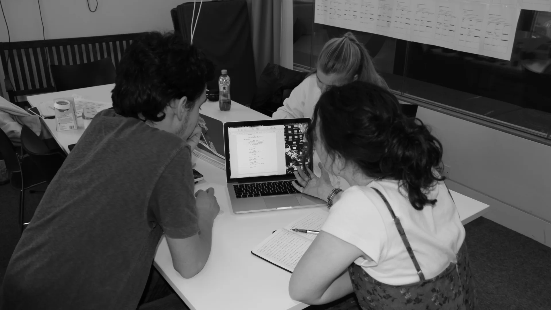 A black and white photo of a group of young people sat around a laptop