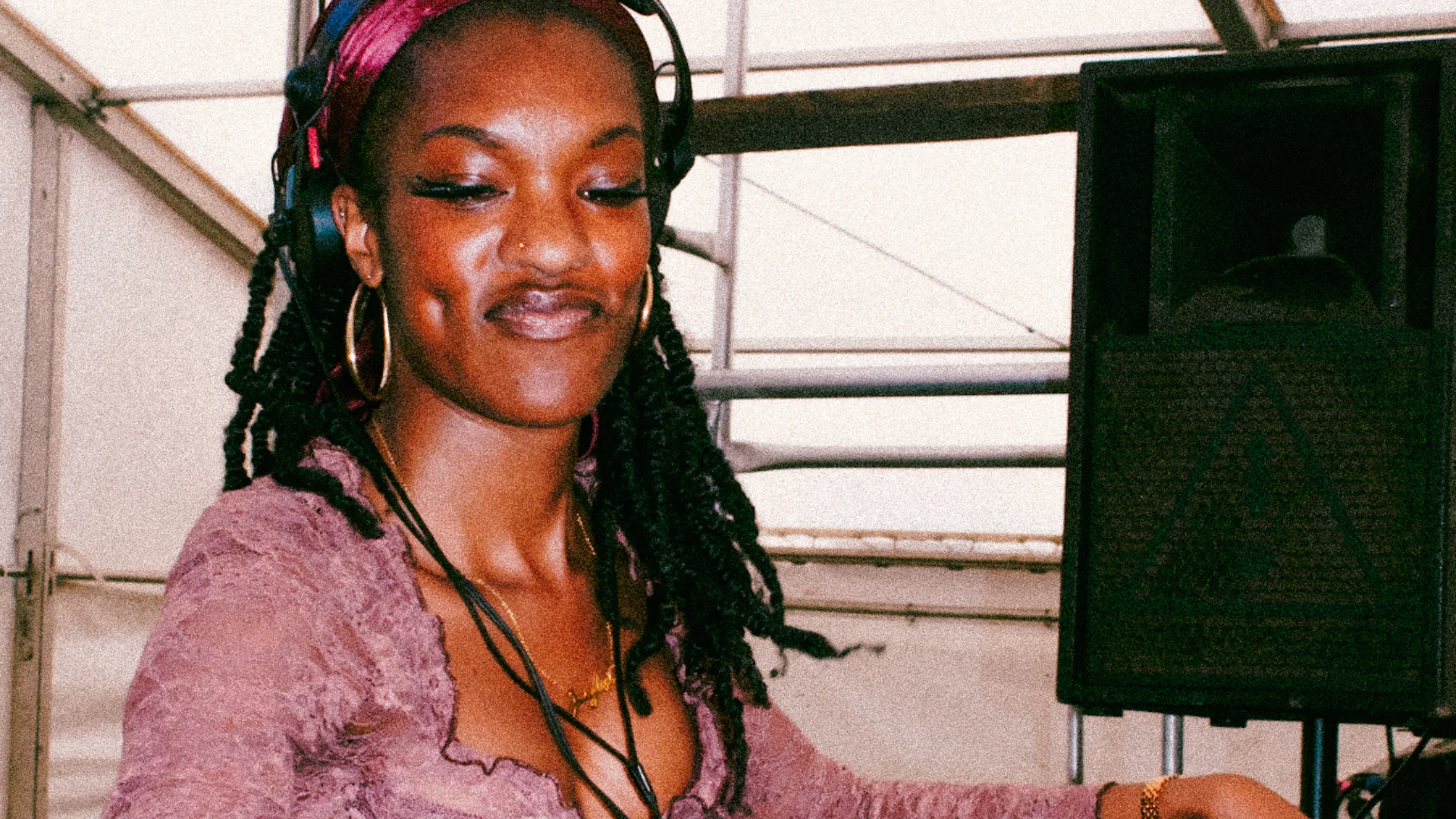 A photo of a young woman with black braids wearing a purple crop top, DJing