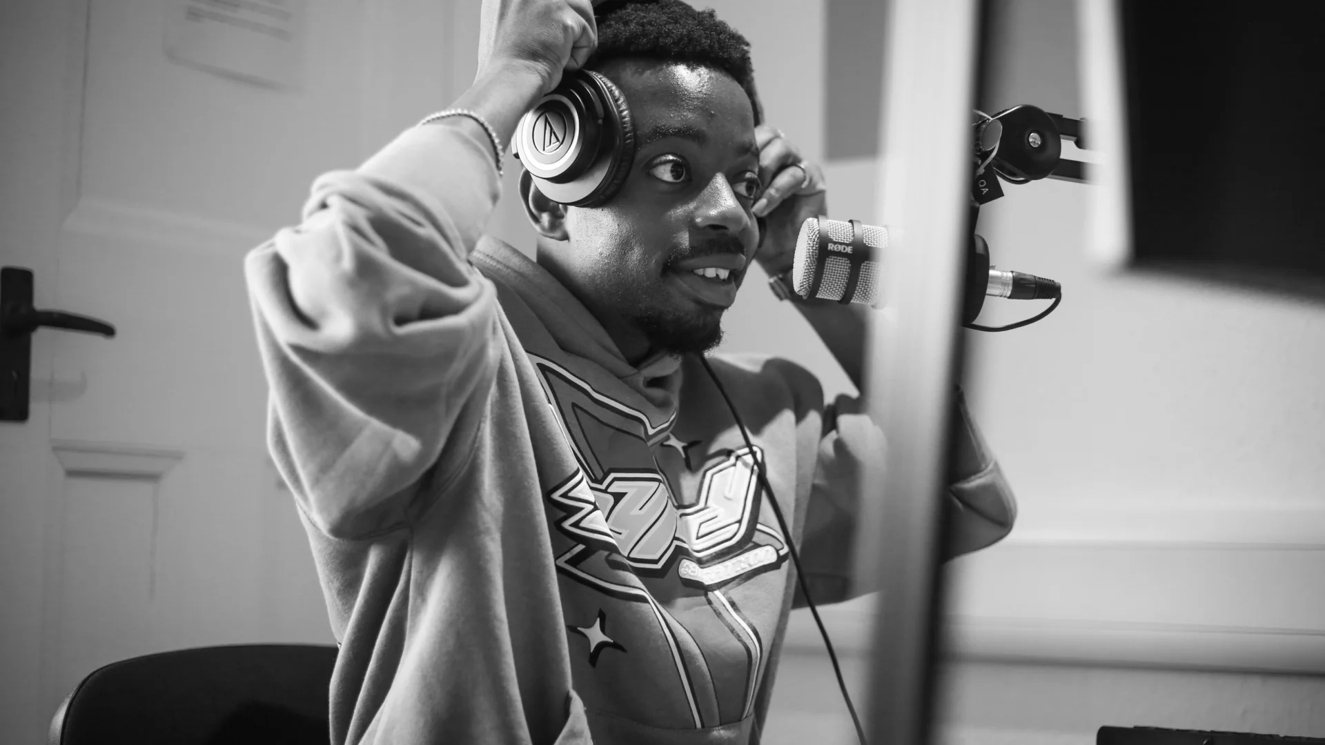 A black and white photo of a young black man wearing a hoodie, holding headphones over his ears.