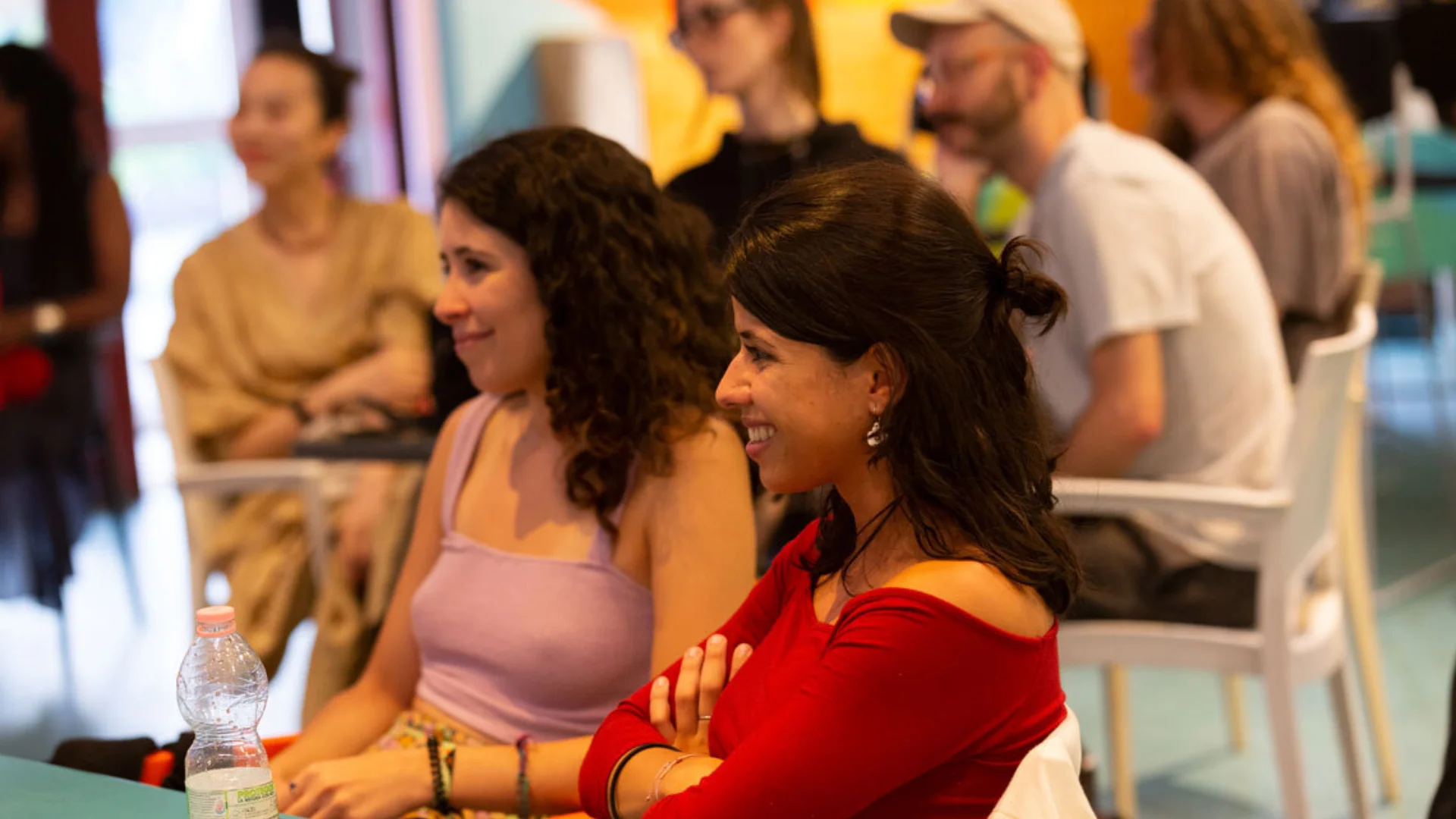 Two women with dark hair sit at a table in the Albany cafe, watching someone off camera and smiling.
