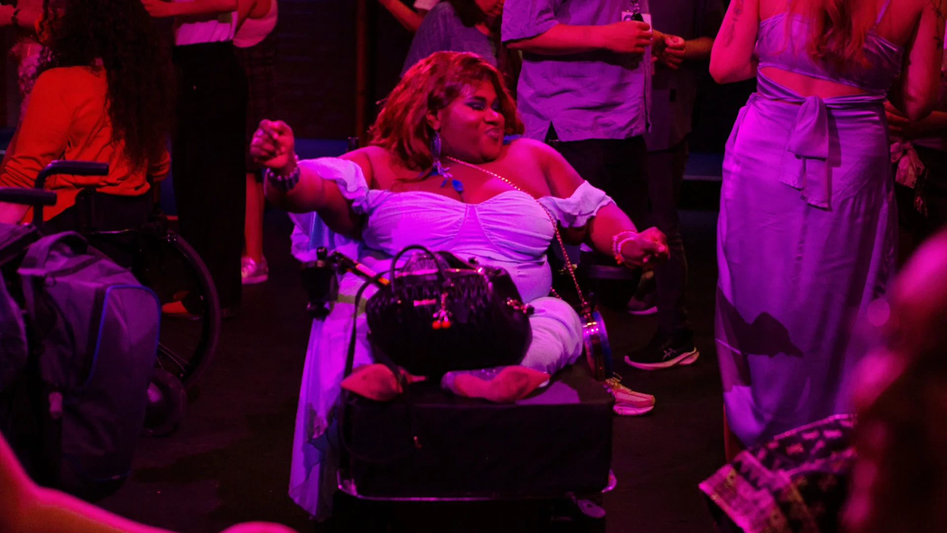 A photo of a woman in a wheelchair wearing a purple ball gown. She is in dancing in the middle of a dancefloor.