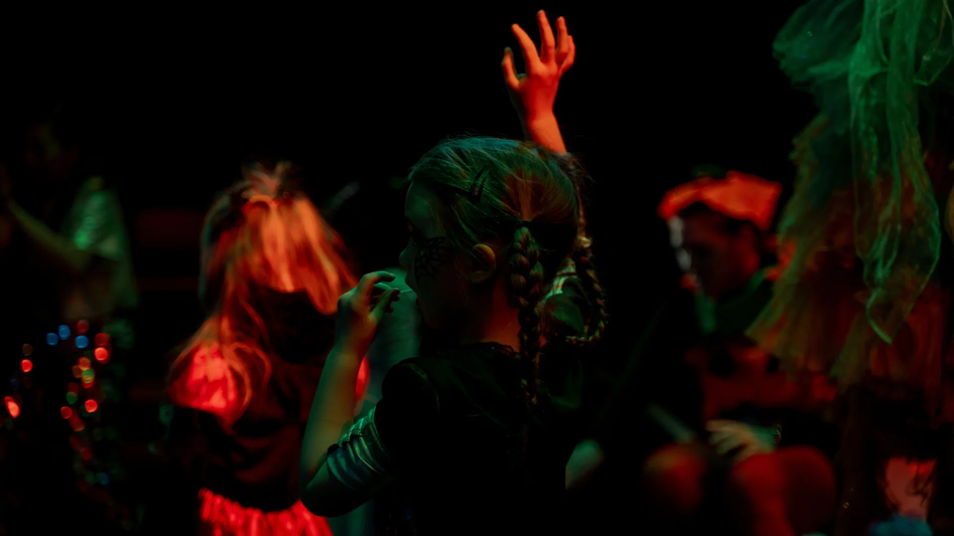 An arty, blurry photo of children dancing, bathed in green and orange light.