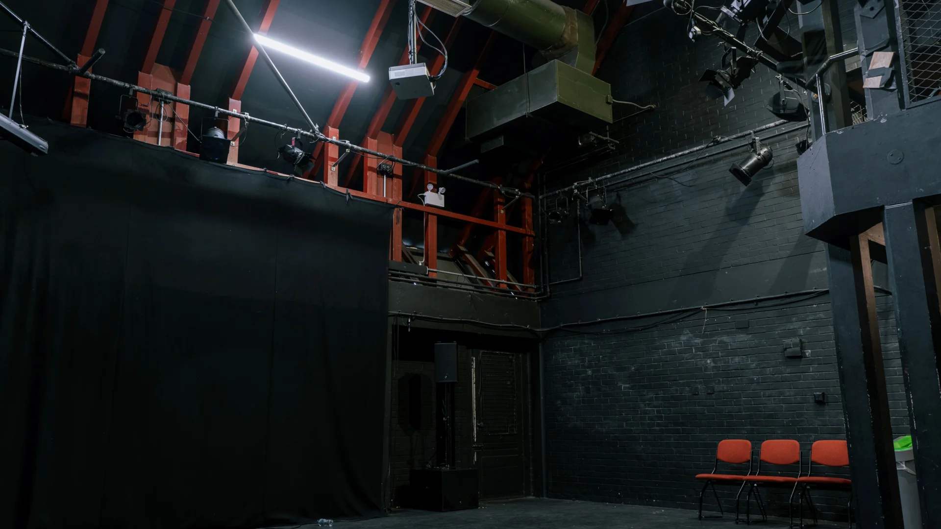 A photo of the Studio at the Albany. Is it a black box space with a black floor and black walls, and a lighting rig on the ceiling.