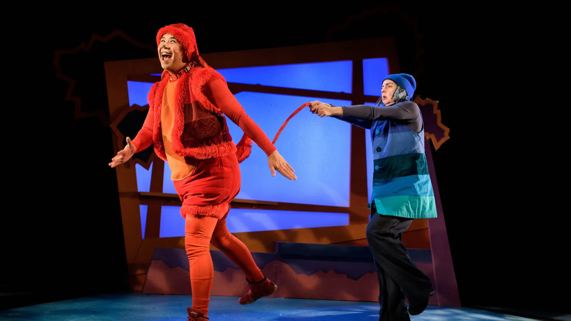 A photo of two performers, one is dressed as an orange dog and the other is holding their tail.