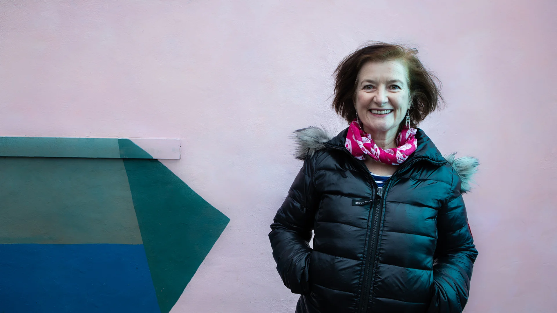 Angela Clerkin - a white woman smiling with brown hair in a pink scarf and black puffer jacket.