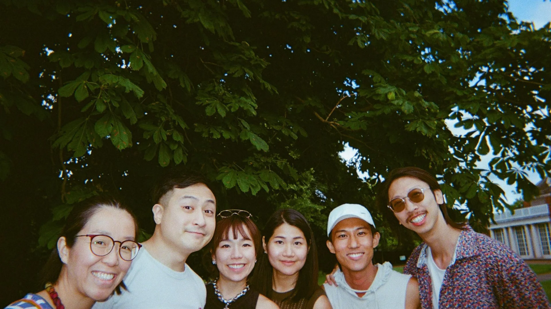 A photo of a group of South East Asian men and women, stood in a line in front of a large tree.