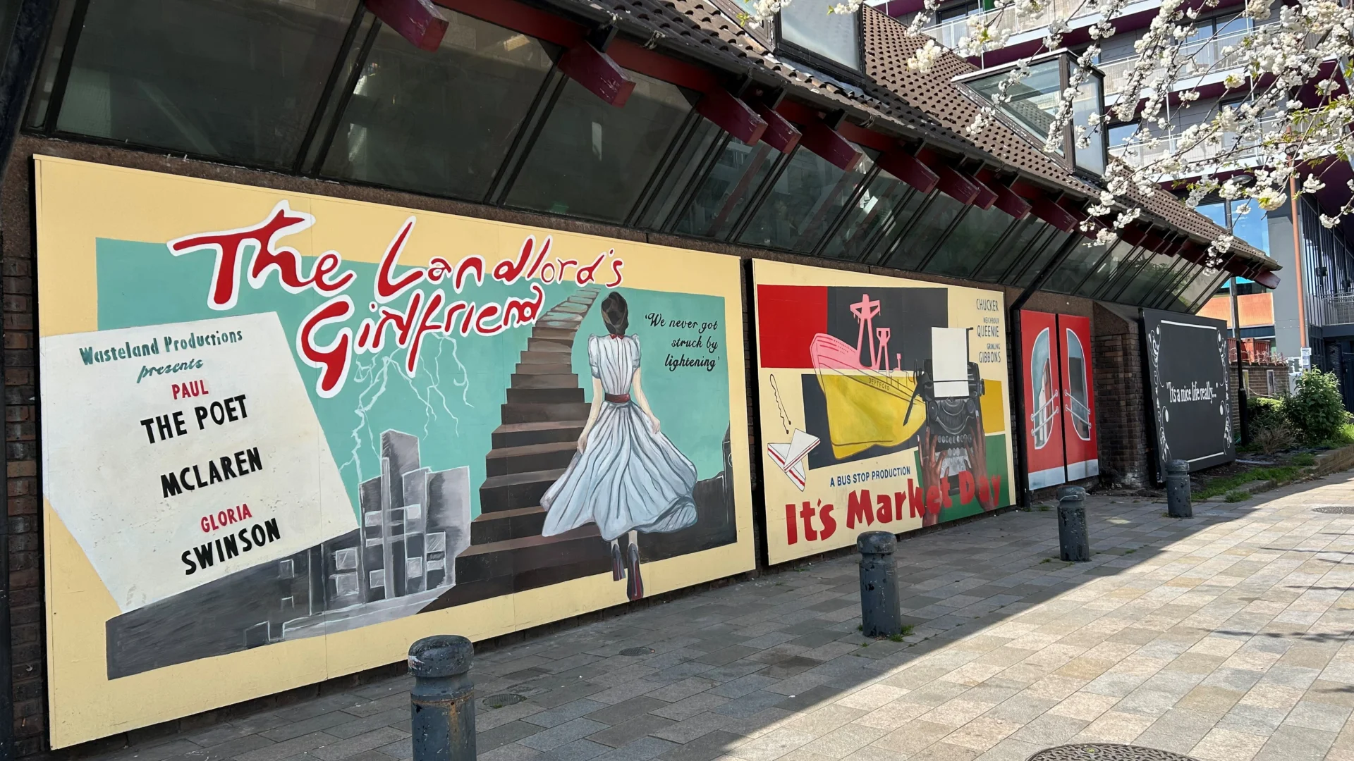 A photo of a bright mural with red text reading 'The Landlord's Girlfriend' and an illustration of a woman in a blue dress walking up a staircase.