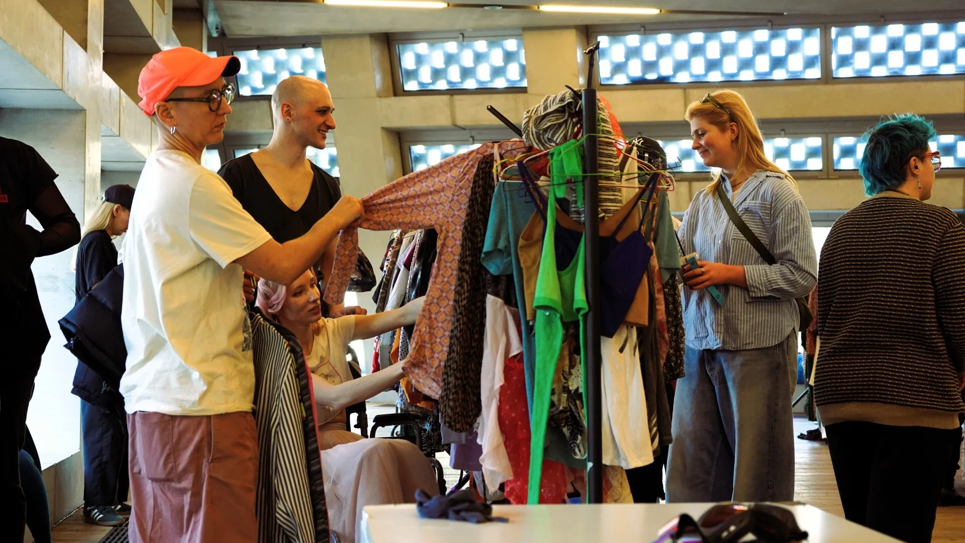A photo of a group of people looking at clothes on a clothes rail.