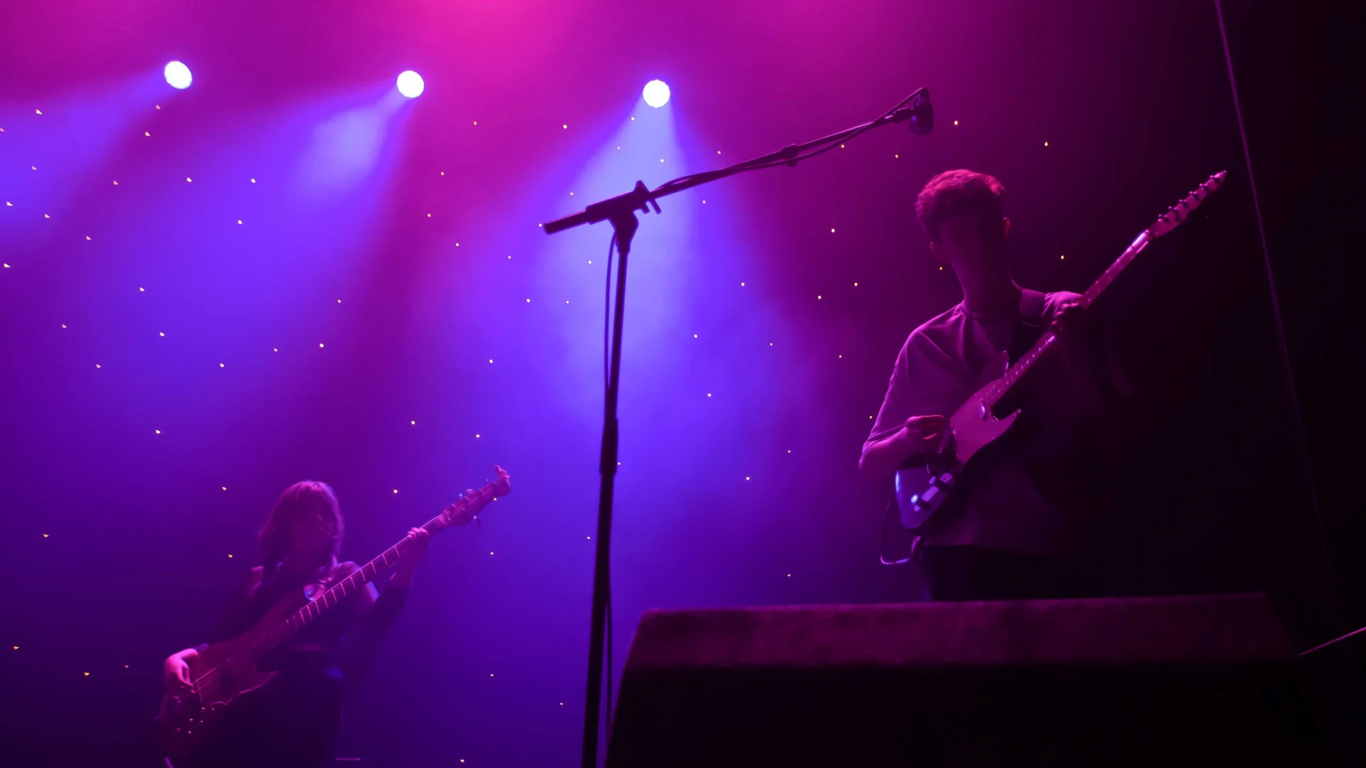 A mic stand and a person on guitar. Pink and purple lighting