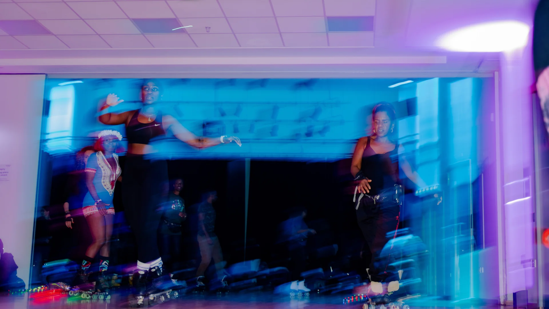 A blurry photo of two people wearing black, roller skating. There is blue and purple light surrounding them.