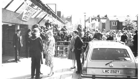 A black and white photograph of Princess Diana having just stepped out of a car at the entrance to the Albany. Behind her there is a crowd watching on.