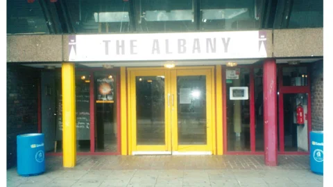 A photograph of the entrance to the Albany, with bright yellow doors and pink pillars.