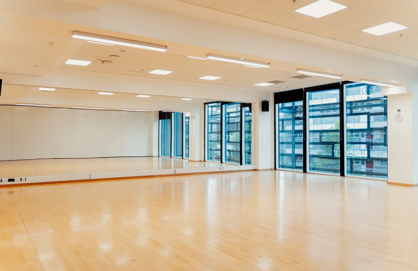 A photo of a dance studio with wooden floors and a mirrored wall. It is light and spacious.