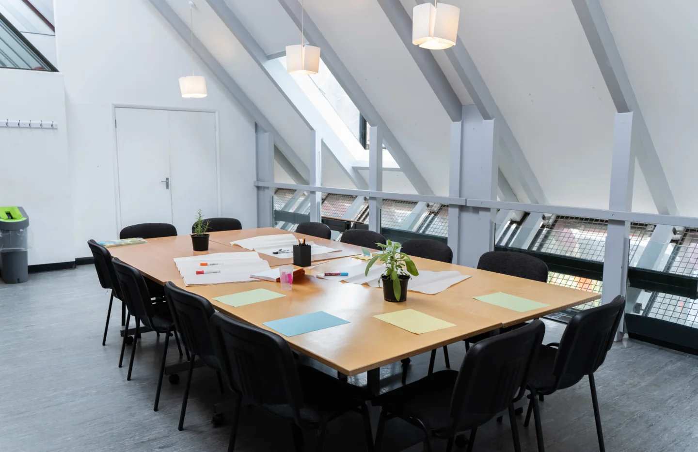 A photo of a meeting room with an empty table and chairs in the middle, set for a meeting with papers, pens and pot plants.