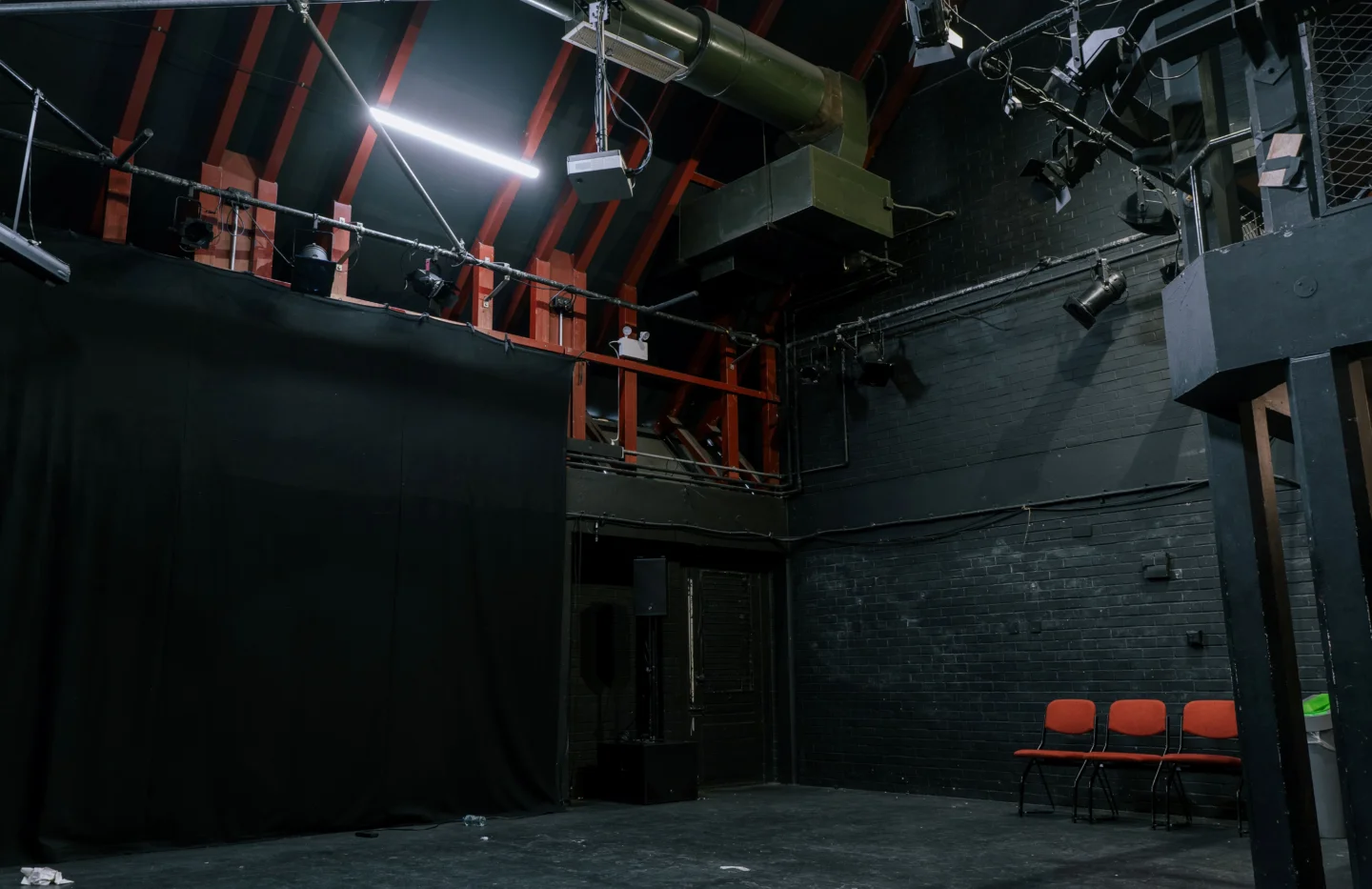 A photo of the Studio at the Albany. Is it a black box space with a black floor and black walls, and a lighting rig on the ceiling.