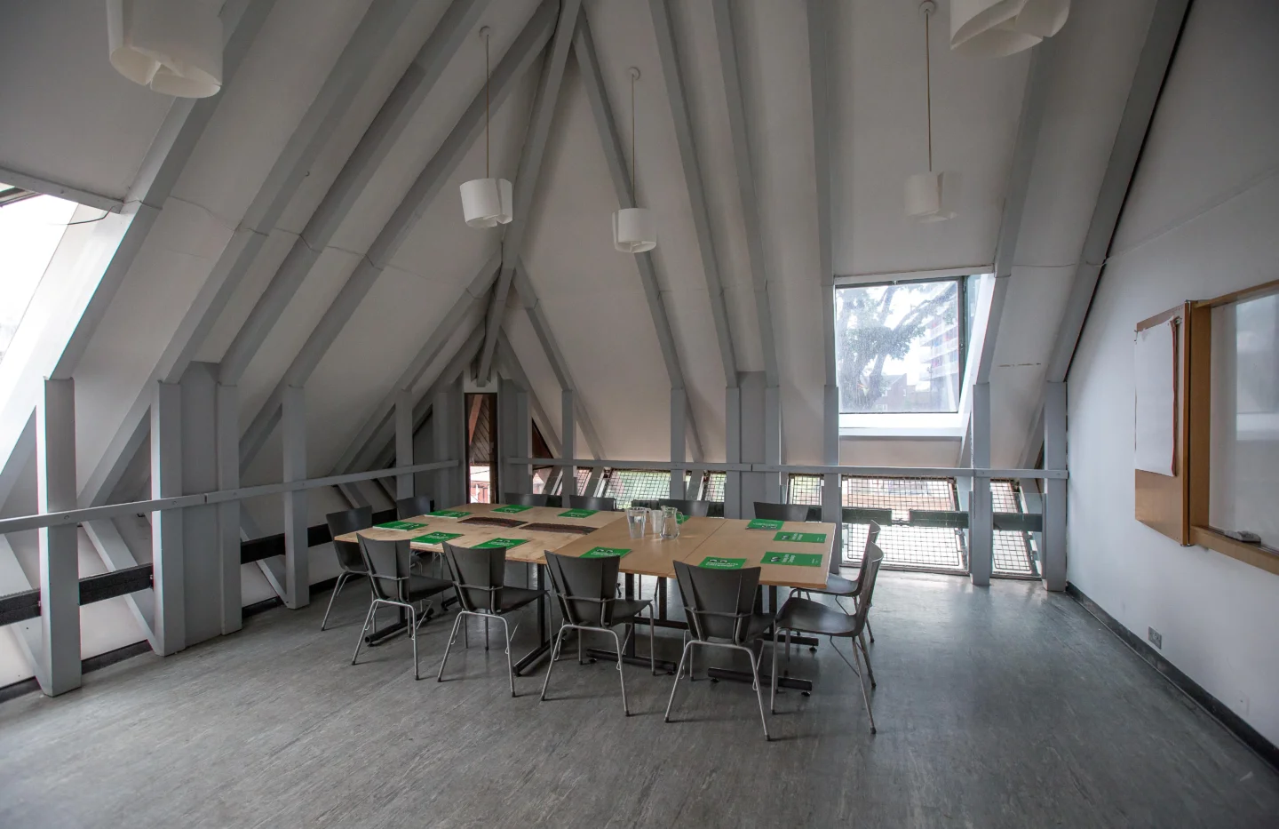 A photo of a meeting room with sloping ceilings and exposed grey beams. In the centre of the room is a table surrounded by chairs, with green booklets laid in front of each chair.