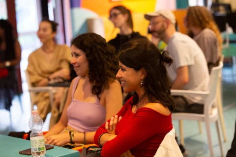 Two women with dark hair sit at a table in the Albany cafe, watching someone off camera and smiling.
