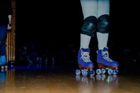 A photo of a person's legs wearing white tights, knee pads and purple roller skates.