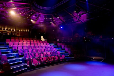 A photo of the Albany with raked seating. The seats are empty, there is purple lighting and the Albany 'A' logo can be seen projected on the back wall.