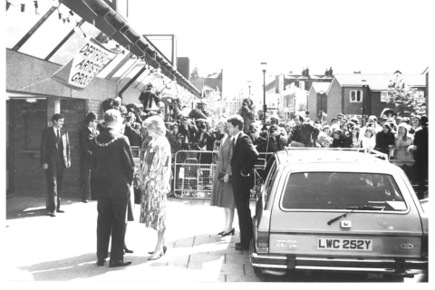 A black and white photograph of Princess Diana having just stepped out of a car at the entrance to the Albany. Behind her there is a crowd watching on.