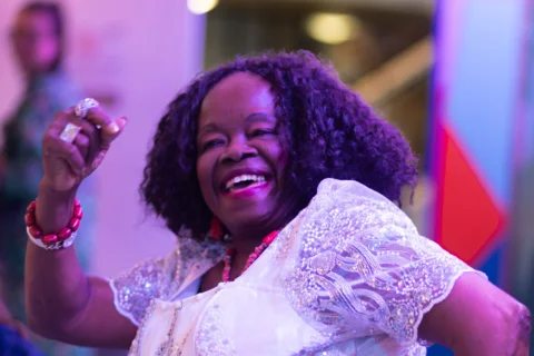 An older woman dancing with an enthusiastic smile on her face. The atmosphere is bright  and colourful and full of joy.