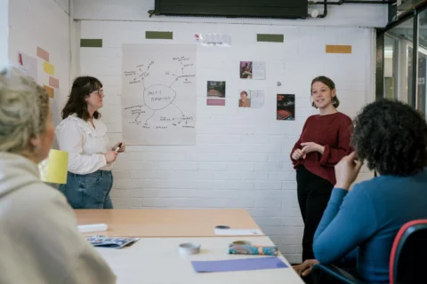 two people standing in front of a wall presenting to a group of gathered people