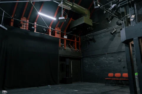 A photo of the Studio at the Albany. Is it a black box space with a black floor and black walls, and a lighting rig on the ceiling.