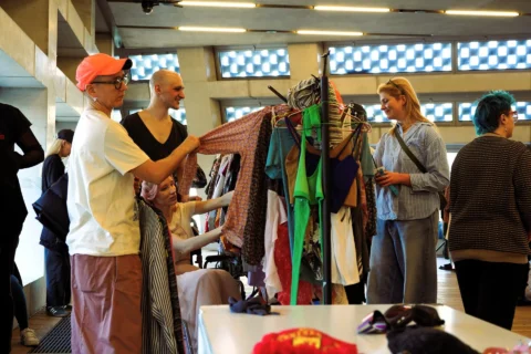 A photo of a group of people looking at clothes on a clothes rail.