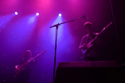 A mic stand and a person on guitar. Pink and purple lighting