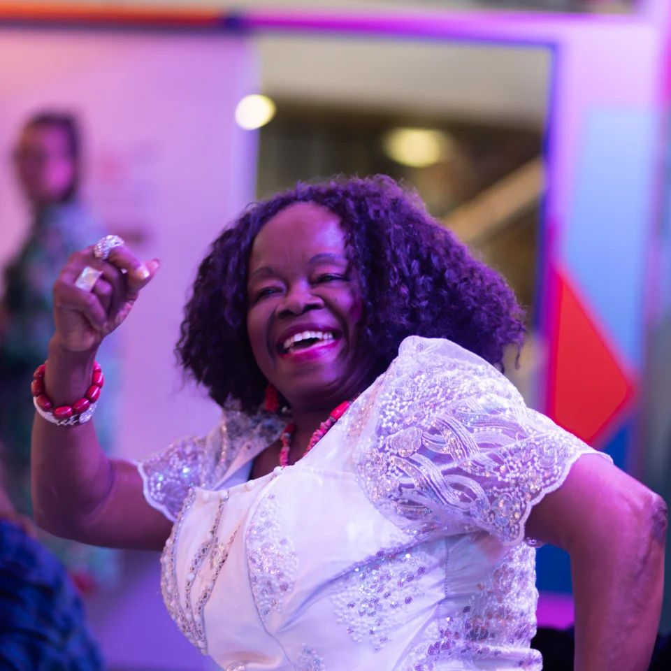 An older woman dancing with an enthusiastic smile on her face. The atmosphere is bright  and colourful and full of joy.